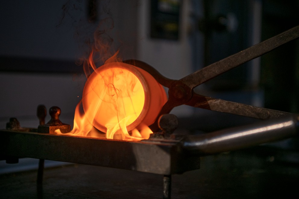 
				Guldet smälter vid 1 250 grader. Dieter fyller sedan den flytande metallen i en gjutform, där den svalnar och blir hård.

			