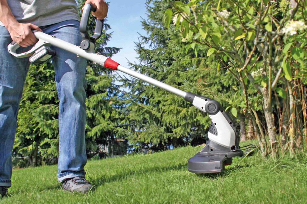 Person använder en batteridriven grästrimmer i trädgården.