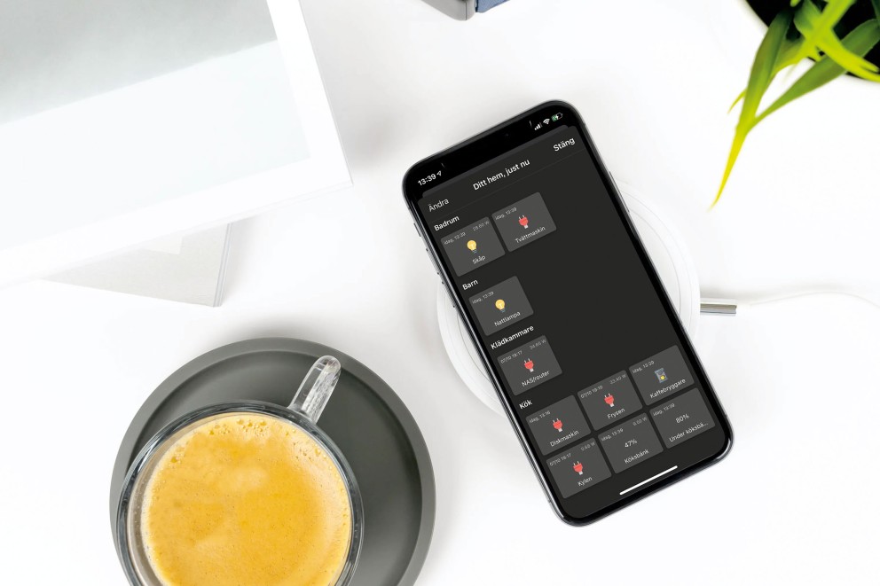 Smartphone med Smart Home-app på en trådlös laddare bredvid en kopp kaffe