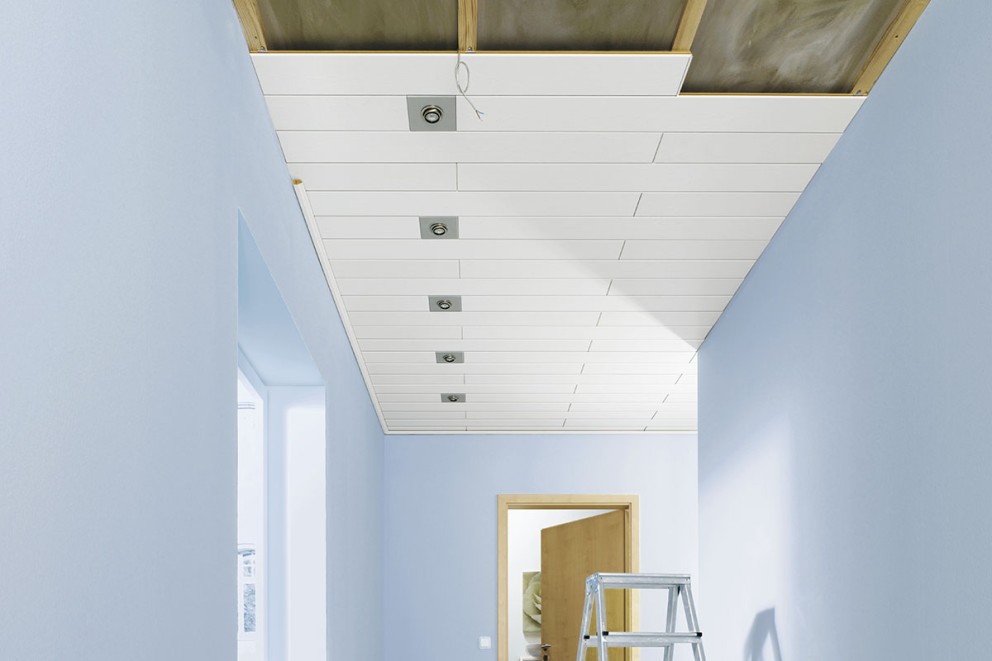 Tak med paneler, infällda spotlights och stege i en hall.
