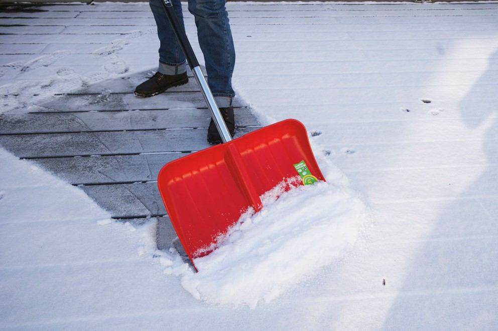 Person skottar snö med en röd snöskyffel på en träaltan