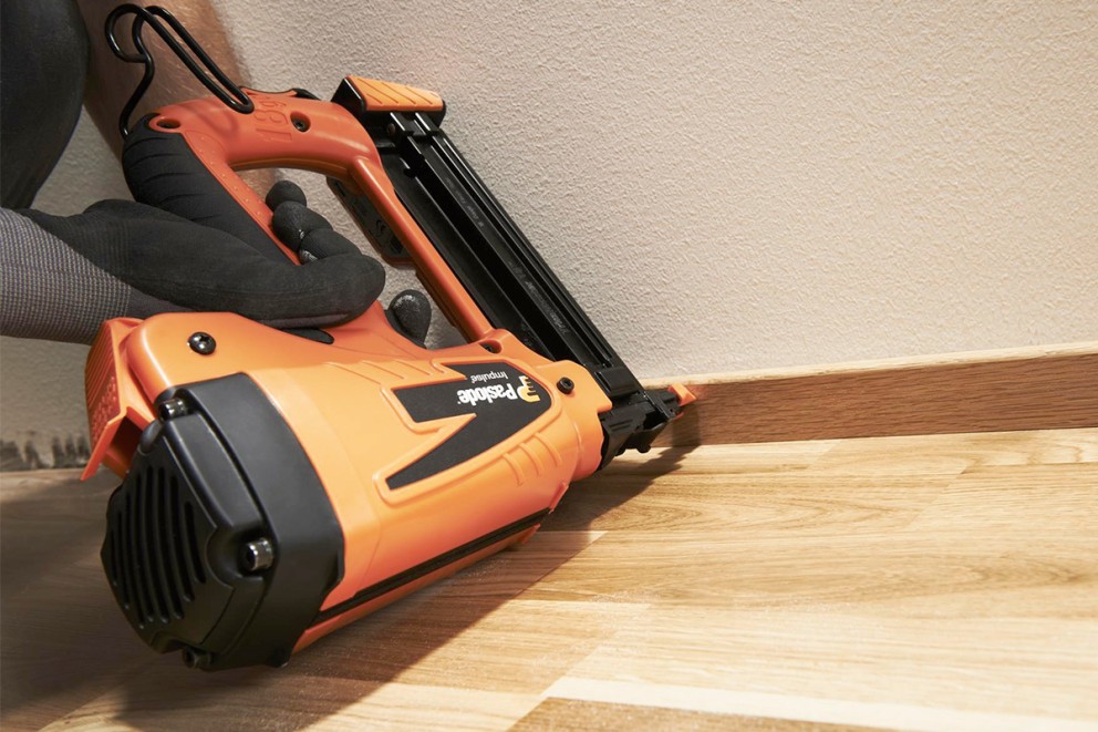 En orange Paslode impulssмістpistol är fäst på en golvsockel.