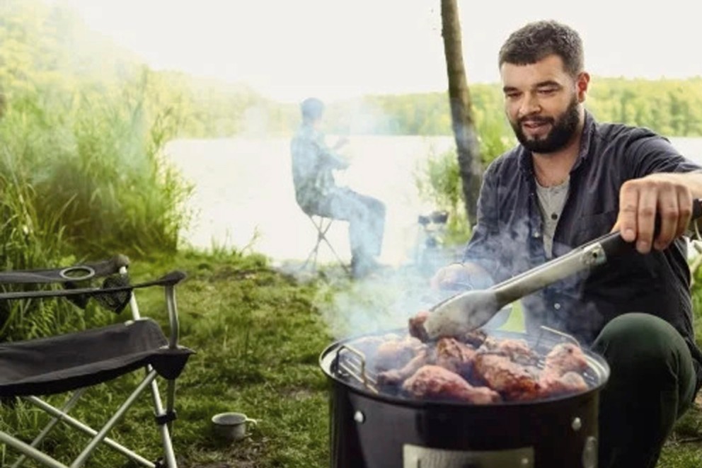 Man grillar kyckling på en kolgrill utomhus.