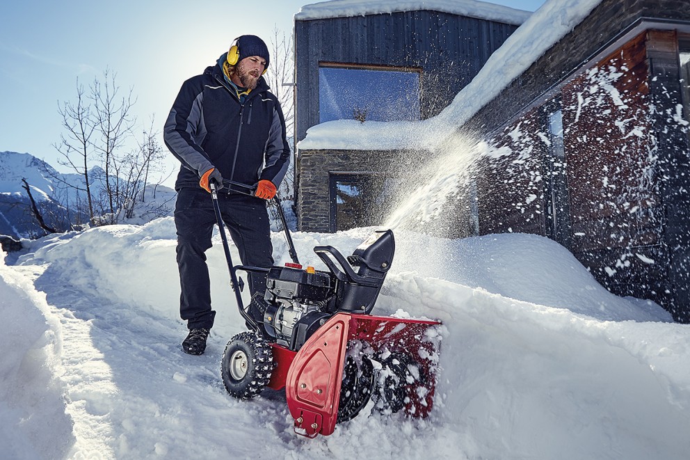 En person använder en snöslunga för att röja snö framför en byggnad.