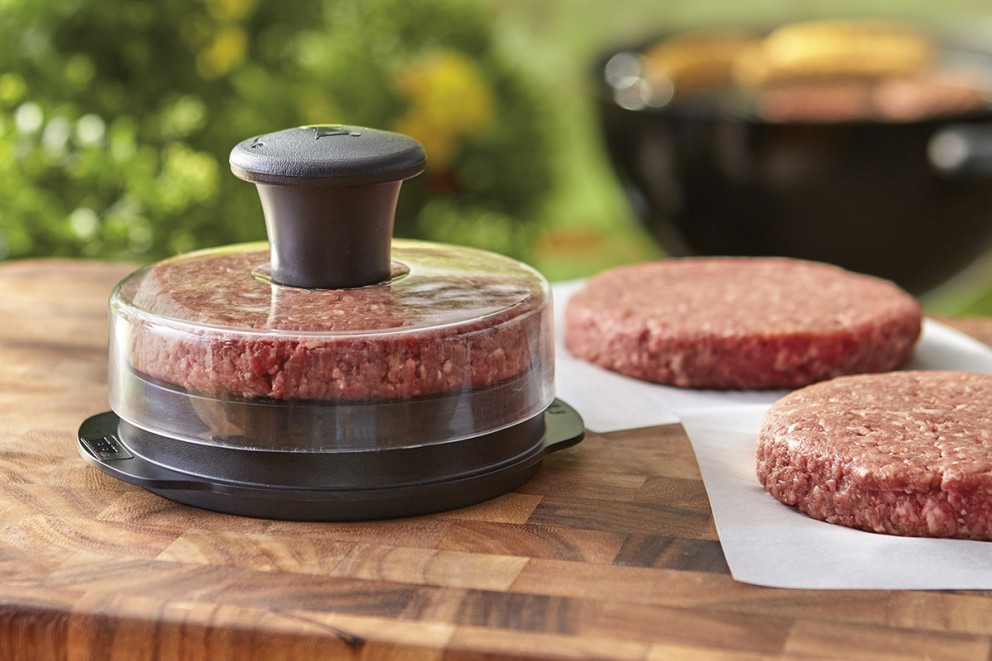 Hamburgarpress med köttfärs och färdiga burgare på en skärbräda