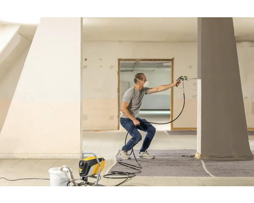 Man använder en färgspruta i ett rum för att måla en pelare