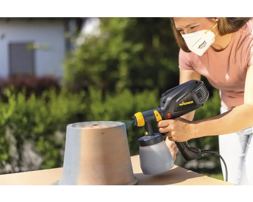 Kvinna sprutar kruka utomhus med färgspraysystem