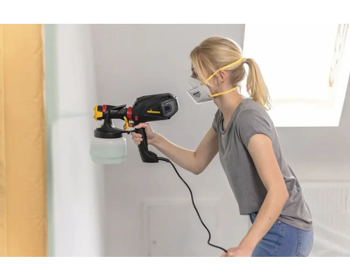 En kvinna sprutar färg på en vägg med en färgspruta.