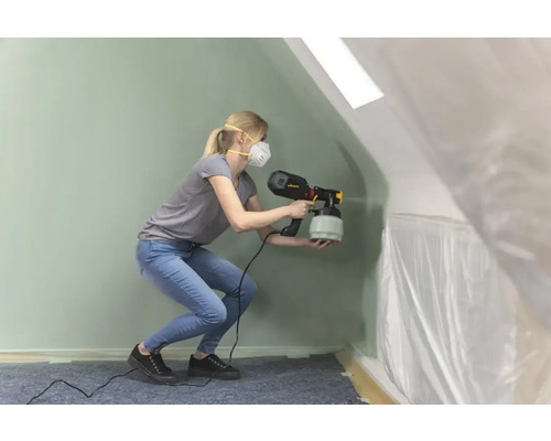 En kvinna använder en färgspruta i ett rum täckt med plastfilm.