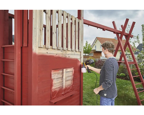 En person sprutar ett lekstuga i trä med en färgsprutpistol