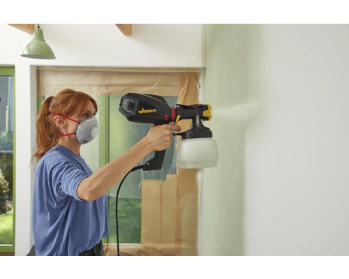 Kvinna målar vägg med Wagner färgspruta