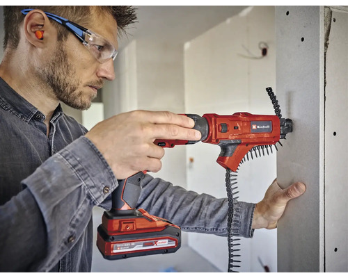 En man använder en Einhell batteridriven gipsskruvdragare för att fästa en gipsskiva. Han bär skyddsglasögon och öronproppar.