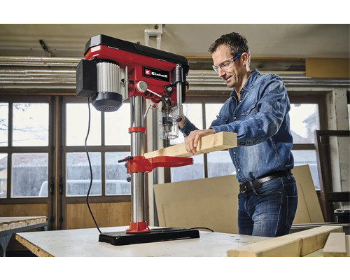 En man borrar en träplanka med en bänkborrmaskin.