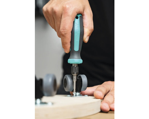 En person fäster ett svänghjul på en träplanka med en skruvmejsel.