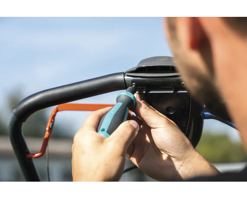 En person fäster handtaget på en gräsklippare med en skruvmejsel.