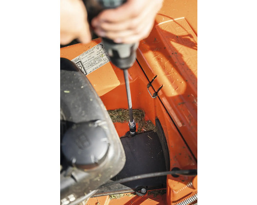 En person använder en skruvmejsel för att reparera en gräsklippare.