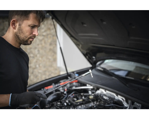 Man med hylsnyckel och öppen motorhuv på en bil