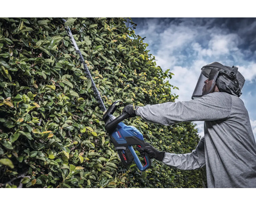 Man med skyddsvisir klipper häck med sladdlös häcksax