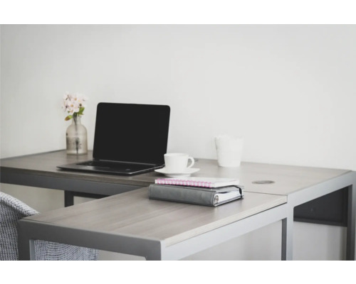 En ljus arbetsplats med skrivbord, laptop, kopp, anteckningsböcker och en liten vas med blommor.