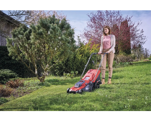 Kvinna använder en röd gräsklippare i trädgården.