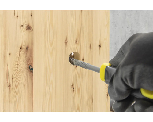 En person använder en trärasp för att förstora ett hål i en träbräda.