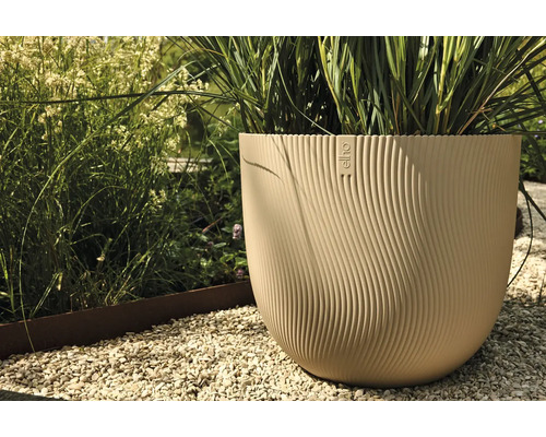 Beige plastblomkruka med Elho-logotyp och vågig textur i trädgården.