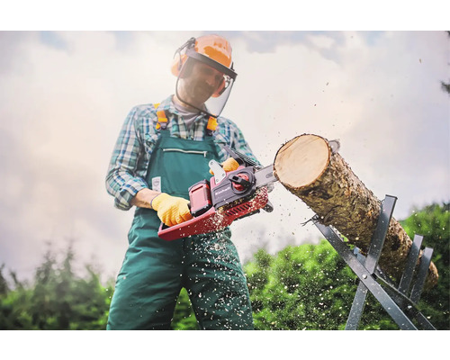 Man med skyddskläder sågar en trädstam på en sågbock med en Einhell motorsåg