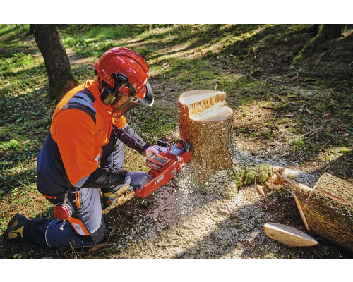 En person med skyddskläder använder en motorsåg på en trädstubbe.