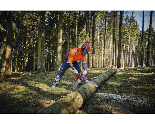 En person i skyddskläder sågar en trädstam i skogen med en motorsåg.