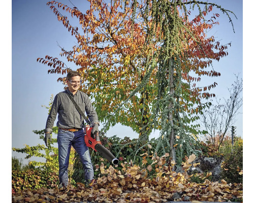 Man använder en lövblås i trädgården för att ta bort löv.