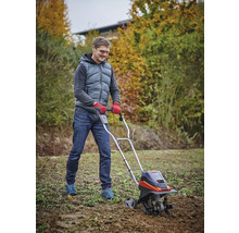 En man använder en jordfräs i trädgården för att bearbeta jorden.