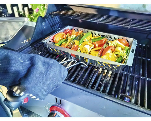 Grönsaker i en grillpanna på en grill, som hålls av en person med en ugnsvante