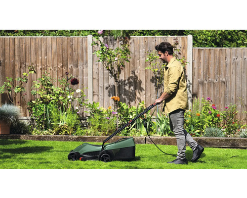 En man klipper gräsmattan med en elektrisk gräsklippare i en trädgård.