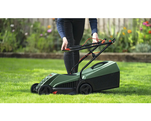 En person använder en grön gräsklippare på en gräsmatta.