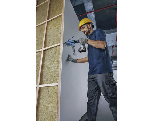 Hantverkare fäster gipsskiva med en skruvdragare med magasin på en vägg