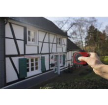 Hand som använder en laseravståndsmätare på ett korsvirkeshus