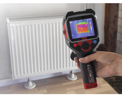 En hand håller en värmekamera framför ett element för att mäta temperaturen.
