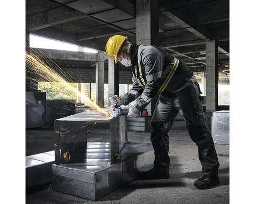 En man med skyddshjälm slipar metall med en vinkelslip, vilket får gnistor att flyga.