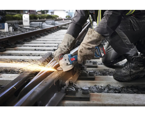 En arbetare skär en järnvägsräls med en vinkelslip, vilket ger gnistor.