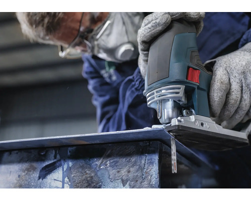 En person med andningsskydd sågar en metallbit med en sticksåg.