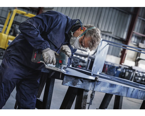 Man med skyddsmask, handskar och hörselskydd sågar en bit metall med en batteridriven sticksåg