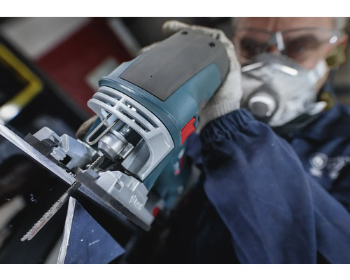 En sticksåg används för att såga material, manövreras av en person med skyddsmask och skyddsglasögon.