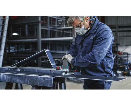 En hantverkare skär en bit metall med en sticksåg. Han bär skyddskläder.