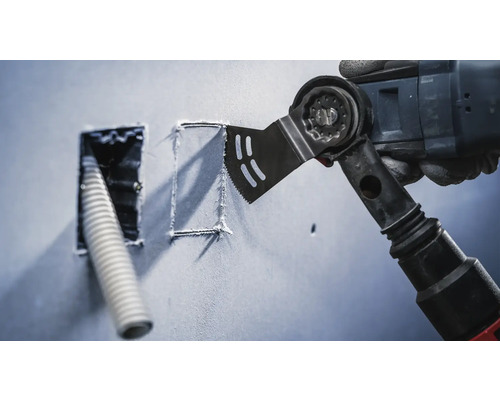 Oscillerande elverktyg skär en fyrkantig form i en vägg bredvid en öppning med en kabel