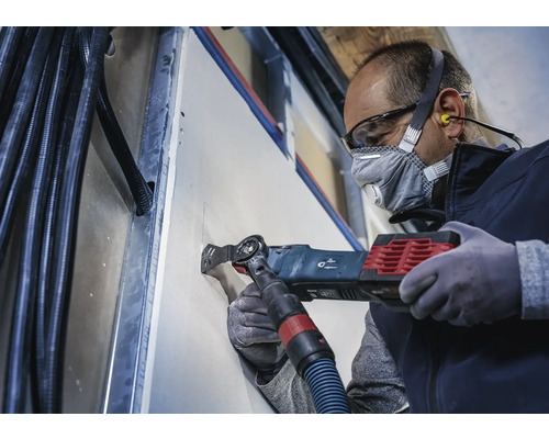 Hantverkare skär ett hål i en gipsvägg med ett multiverktyg