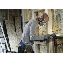 Hantverkare med andningsskydd och skyddsglasögon som arbetar med ett multifunktionsverktyg i ett skalbyggnad