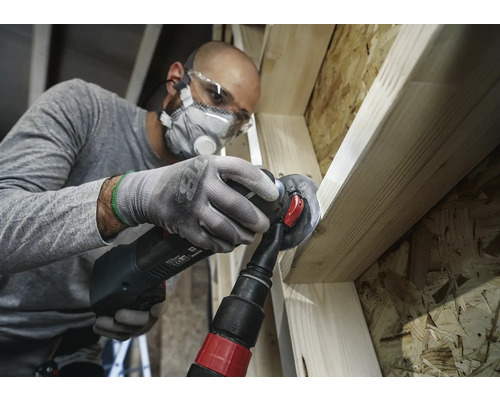 Hantverkare bearbetar trä med ett multifunktionsverktyg, inklusive dammutsugning, skyddsglasögon och andningsskydd.