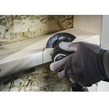 En person sågar en träplanka med ett multifunktionsverktyg.