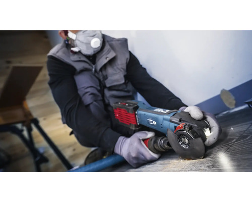 Hantverkare använder en vinkelslip med dammutsug på ett trägolv