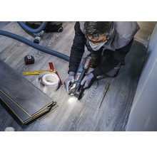 En hantverkare skär laminat med en multifunktionell verktygsmaskin för att skapa en utskärning för ett rör. Verktyg som ett måttband och en penna finns till hands.